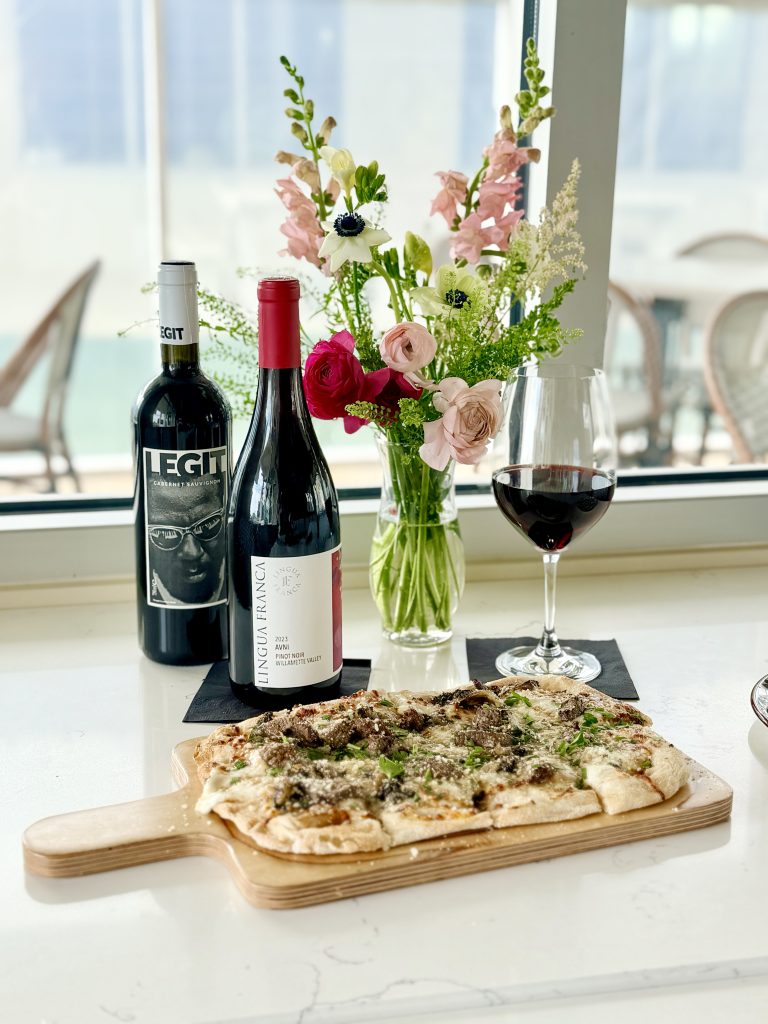 IMG_2727 copy Home dining at Field’s Italian in Pass Christian with LEGIT Cabernet Sauvignon, a red-capped bottle, pink flowers, and pizza on the table.
