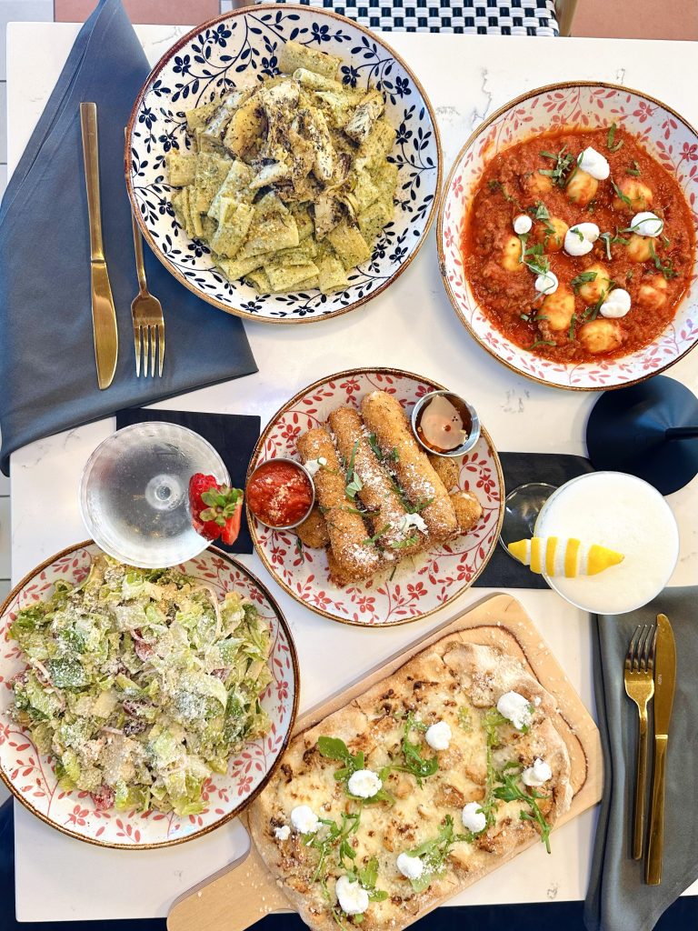 IMG_3355 copy Plates of house-made pasta and Italian specialties with a red marinara bowl, green pesto pasta, and breadsticks on the table at Field’s Italian Pass Christian.