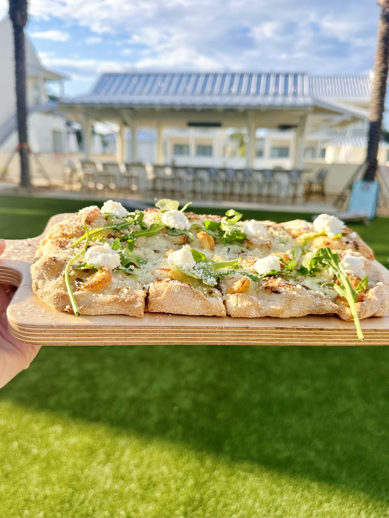 IMG_3437 copy Golden-brown Italian flatbread with fresh green arugula and crumbled cheese on a board, with Pass Christian, MS, in the background.