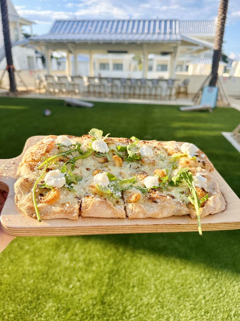 IMG_3438 copy Golden wood-fired pizza topped with arugula, ricotta, and parmesan sits on a board over a green lawn, with Field’s Italian Pass Christian vibes.