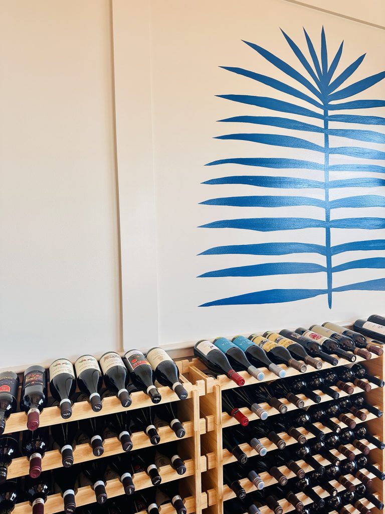 wines A wall mural with blue palm lines above wooden wine racks filled with bottles, bringing Italy’s bold flavors from Napa Valley and Tuscany to home in Pass Christian.